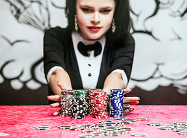 Ein weiblicher Dealer, der Jetons über einen Casino Tisch schiebt.